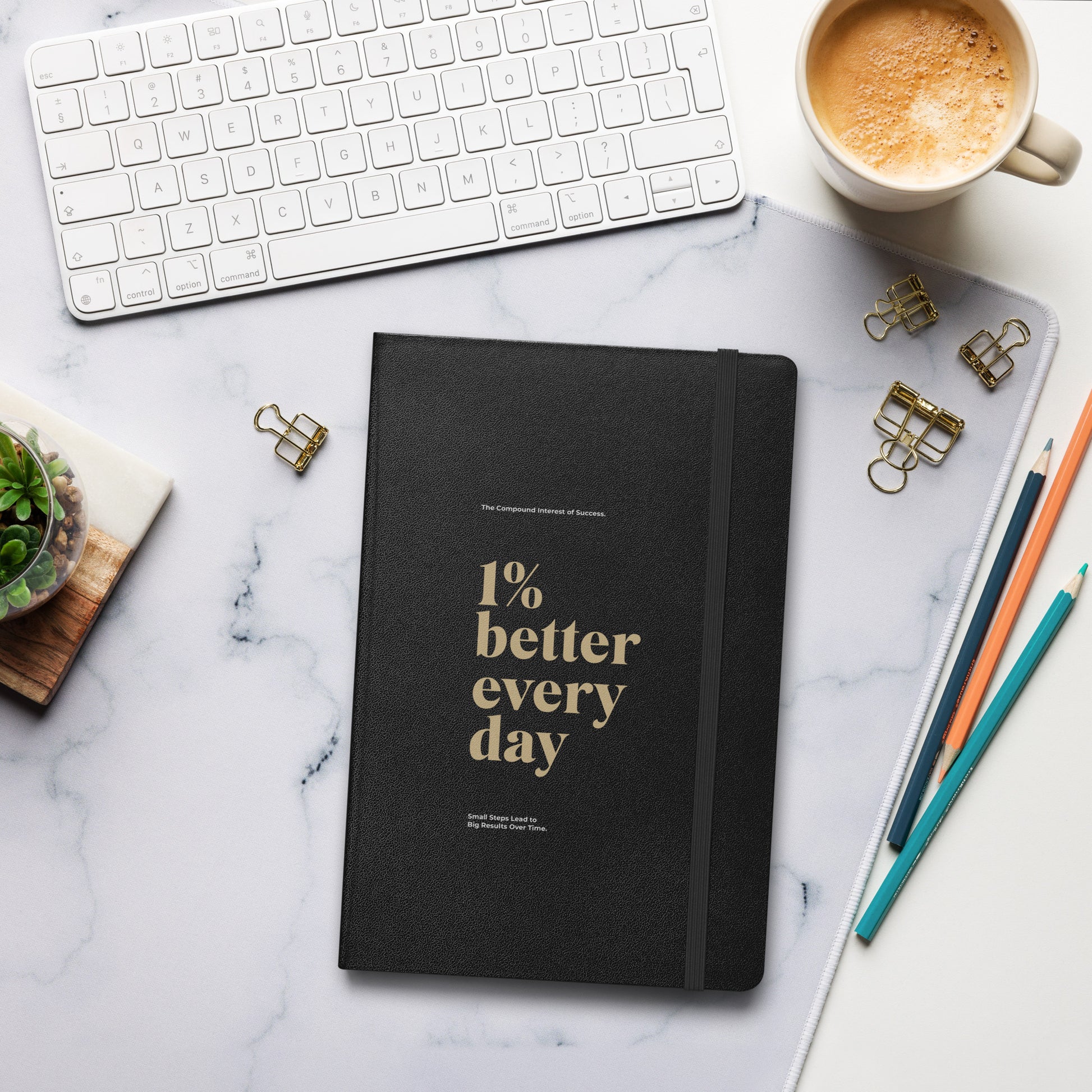 Black notebook with '1% better every day' on a marble desk with office supplies. Growth Mindset & Productivity Journal For Speaker, leaders, executives, professionals and business owners by wear grit brand