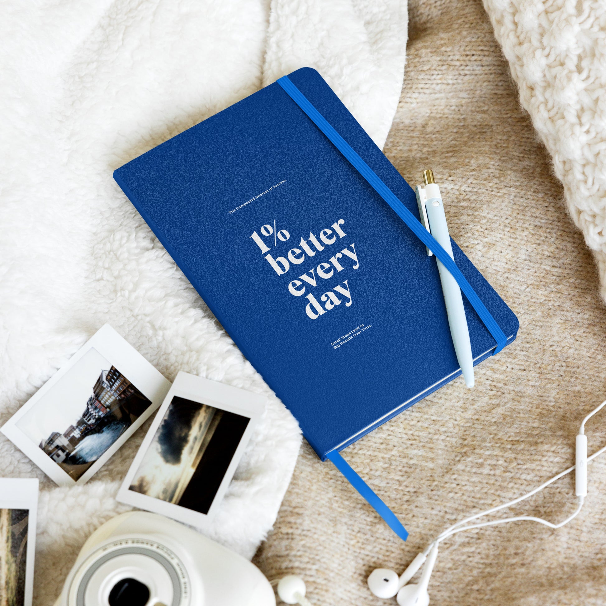 Blue notebook with '1% better every day' on a marble desk with office supplies. Growth Mindset & Productivity Journal for speakers, leaders, executives, professionals and business owners by wear grit brand