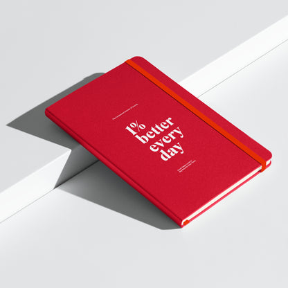 red notebook with '1% better every day' on a marble desk with office supplies. Growth Mindset & Productivity Journal For Speaker, leaders, executives, professionals and business owners by wear grit brand