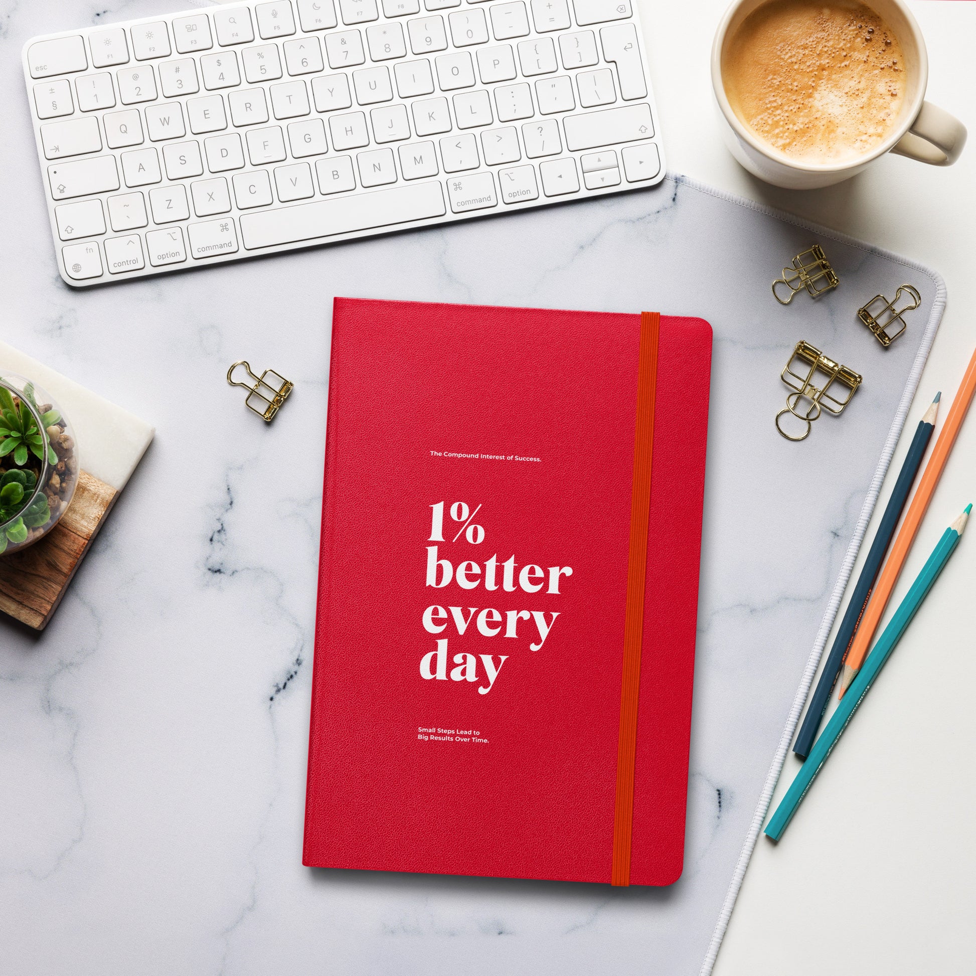 Red notebook with '1% better every day' on a marble desk with office supplies. Growth Mindset & Productivity Journal For Speaker, leaders, executives, professionals and business owners by wear grit brand