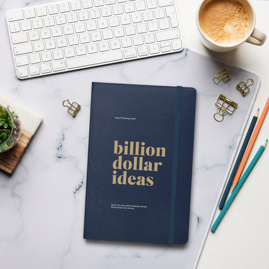 Navy matte journal on a desk with the text "Billion Dollar Ideas" stamped on the cover, designed by Wear Grit for entrepreneurs to write down business strategies and goals


